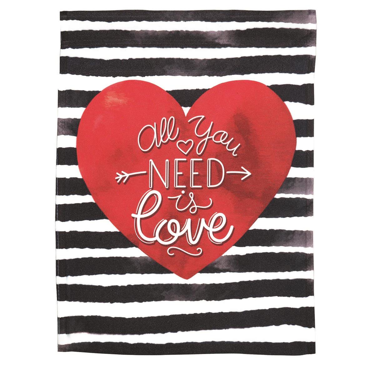 All You Need Is Love 13x18 printed Valentine's garden flag hanging from a stand in a garden.